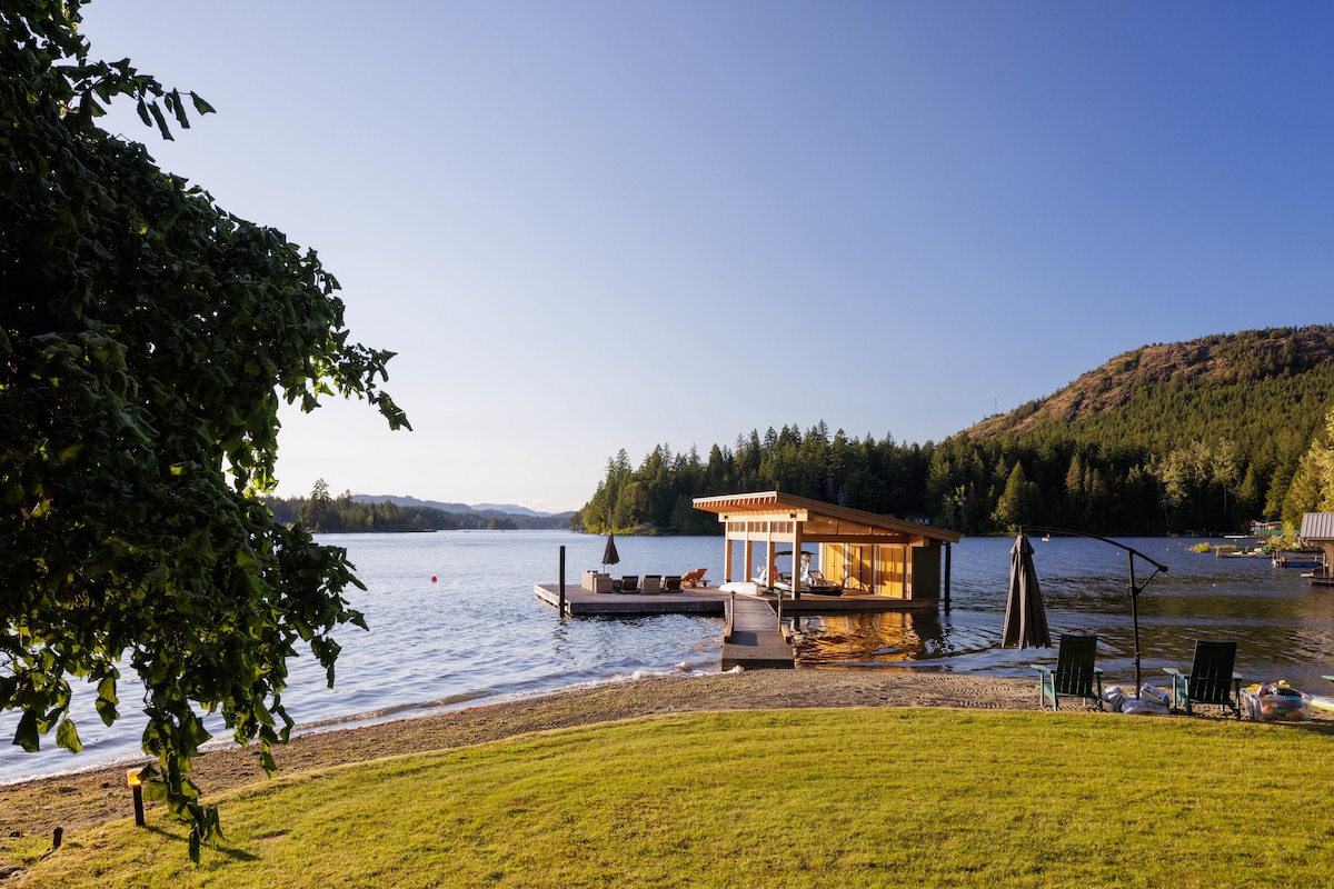 Shawnigan Lake on a clear day, with the boathouse, dock, and grass beach in the foreground