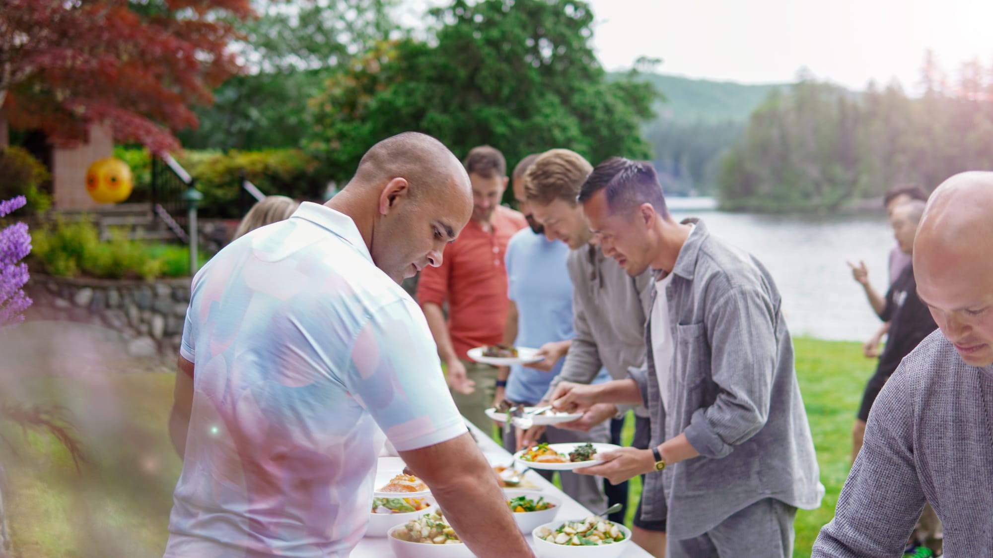 Group serving themselves at a chef-prepared buffet outdoors with the lake behind them